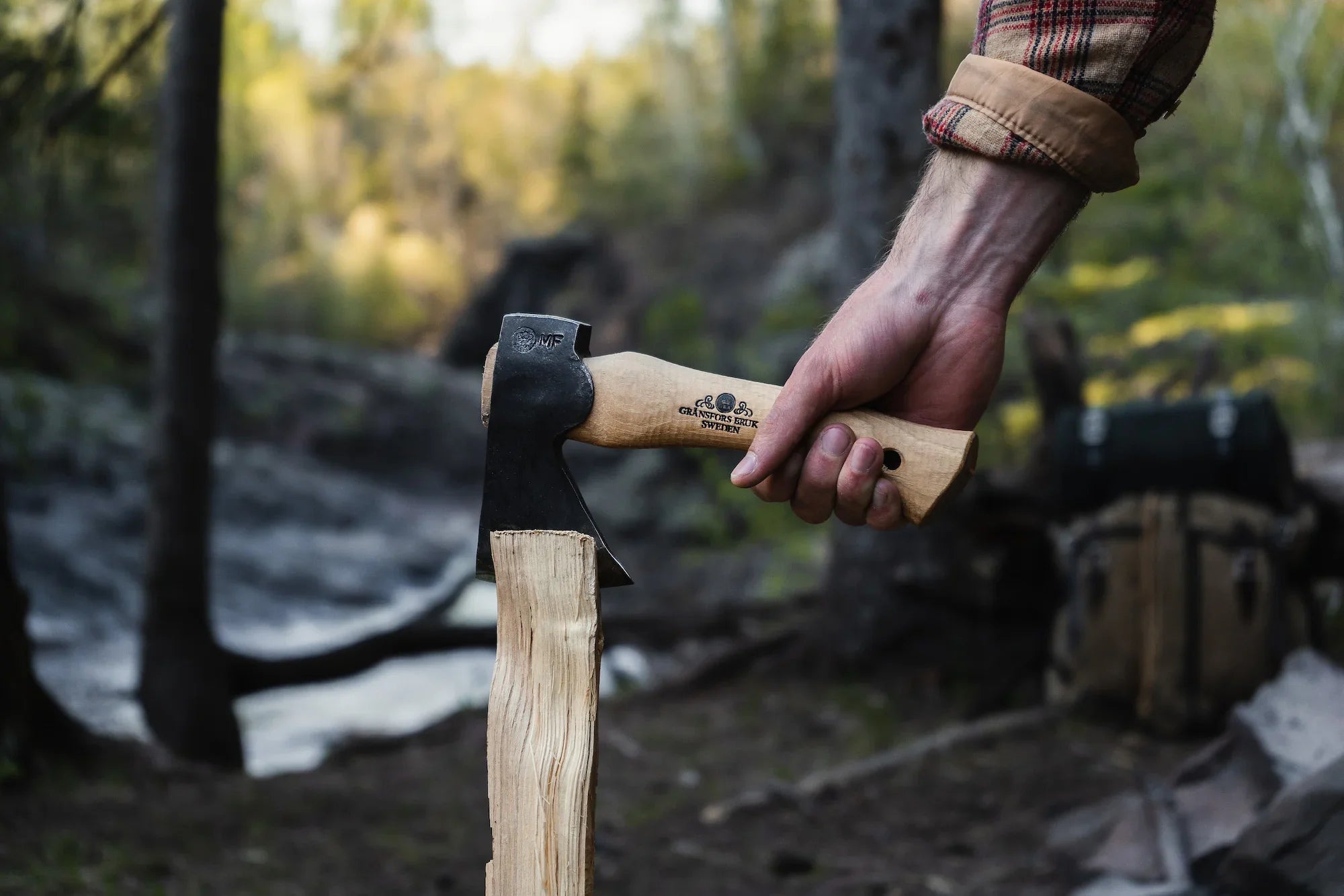 A man splitting wood in a forest with a waterfall in the background. 