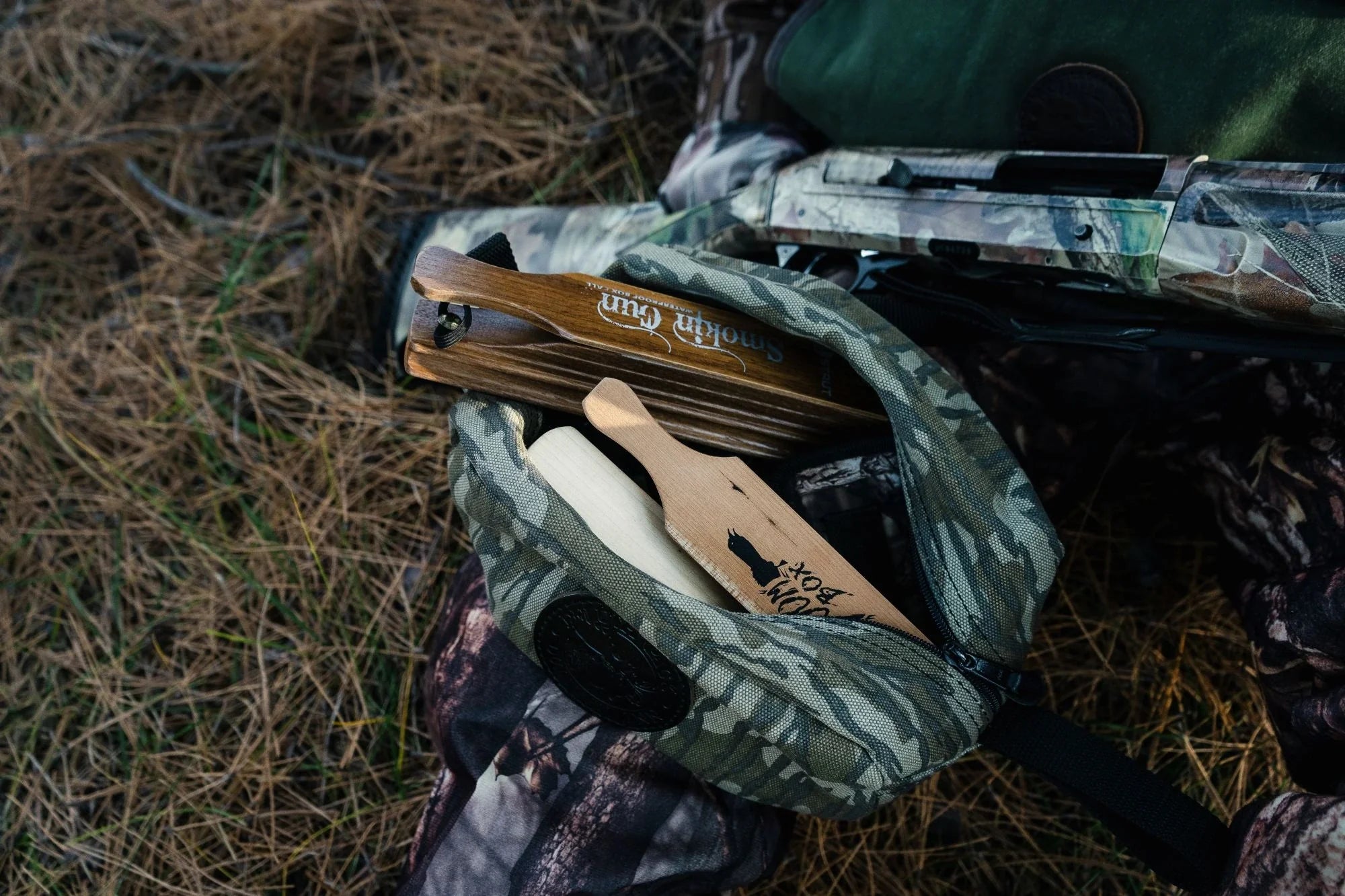A camo Duluth Pack Grab-N-Go open with turkey hunting calls with hunting gear in the background.