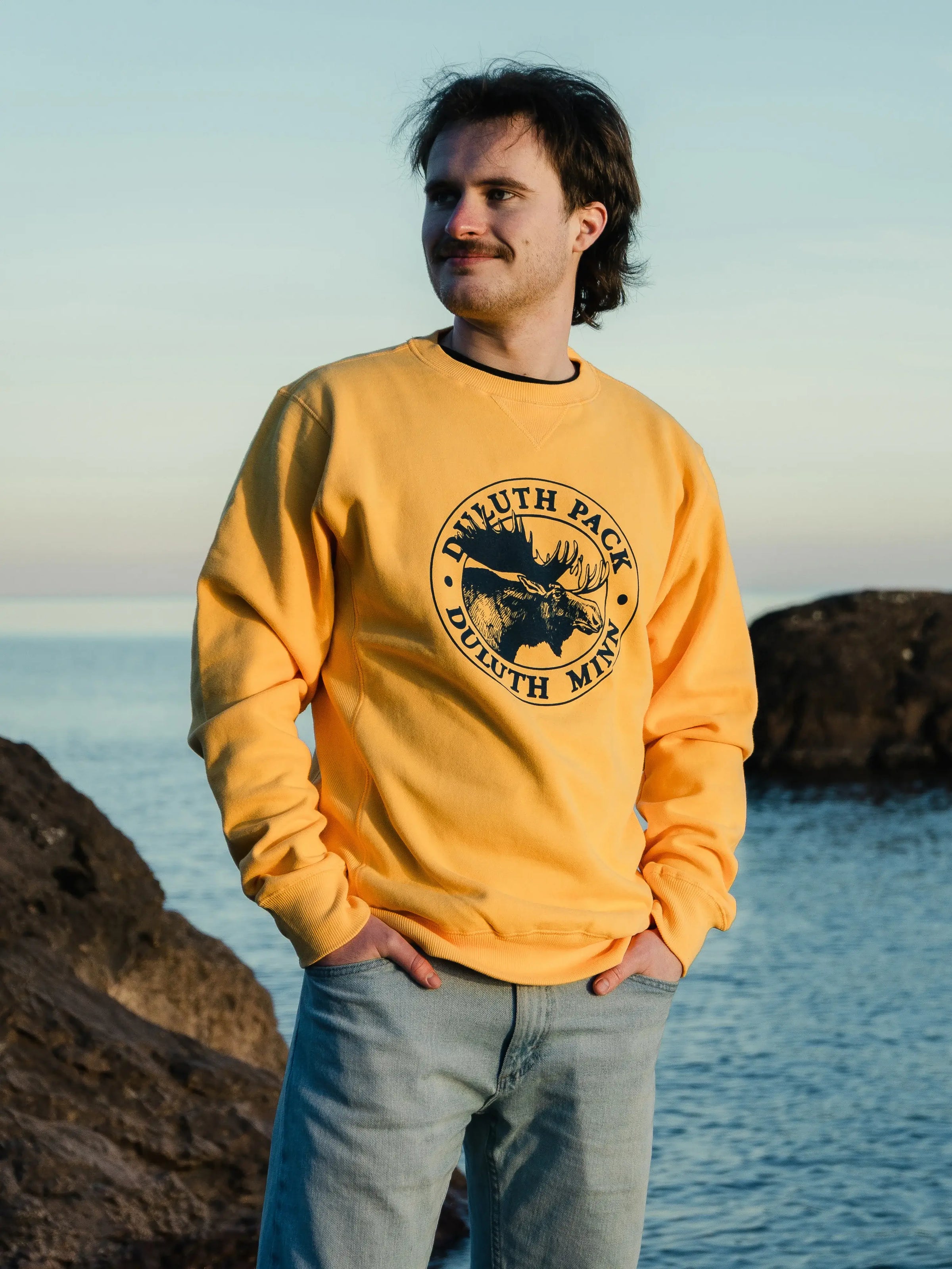 Man wearing a yellow Duluth Pack Crewneck with a lake in the background