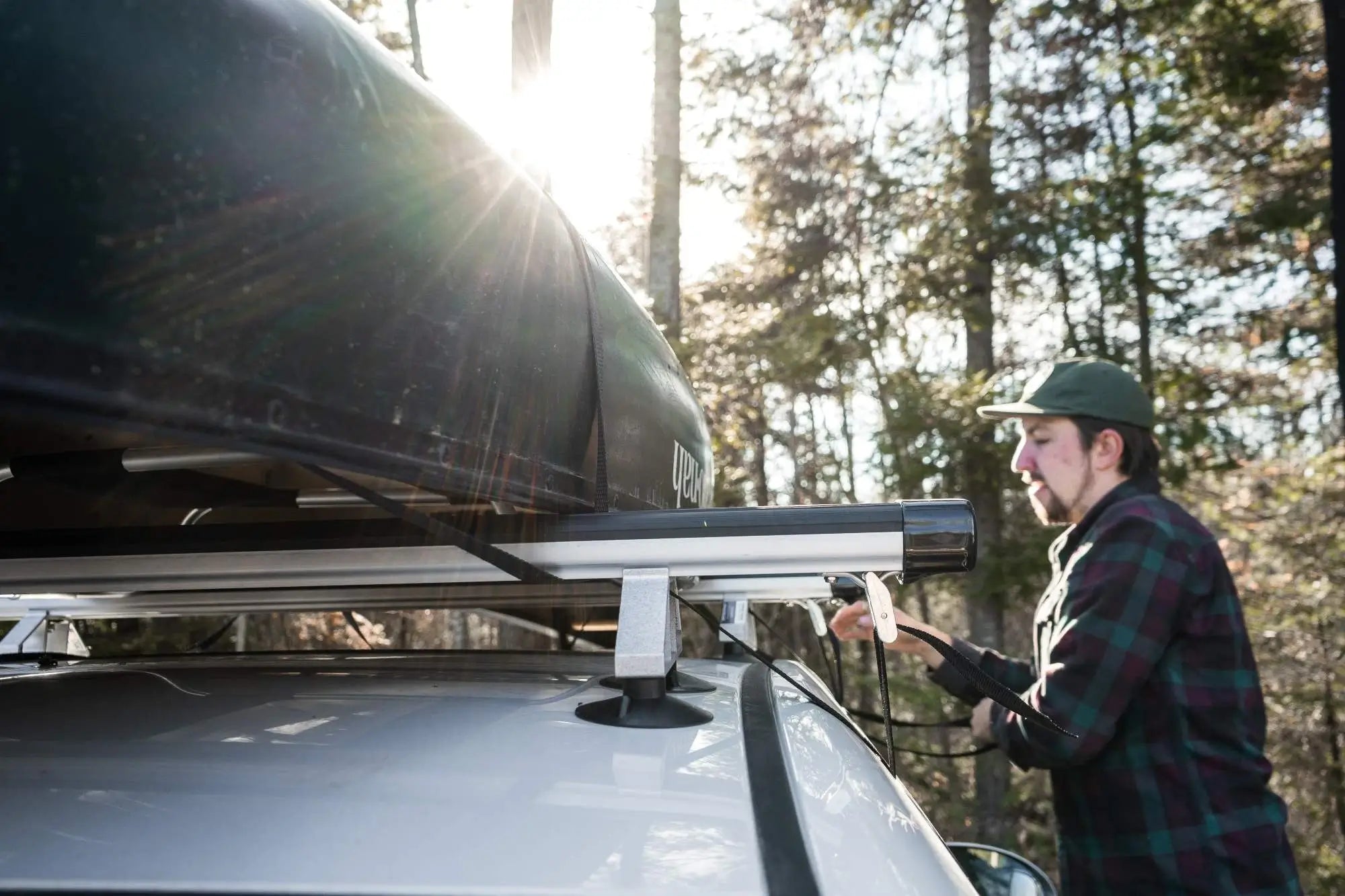 A man wearing a Duluth Pack Flannel attaching a canoe to a Spring Creek Manufacturing Spring Creek DIY Suction Cup Rack Kit onto the man's car with a forest in the background. 