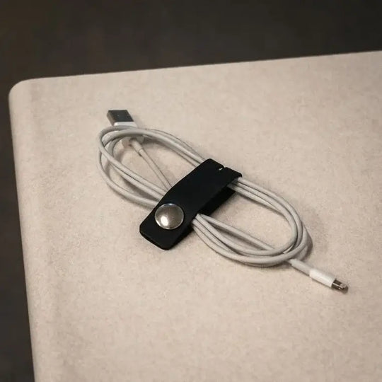 Leather Cord Organizer As Seen From The Side On A White Background Used On A Phone Charging Cable, Resting On A Surface