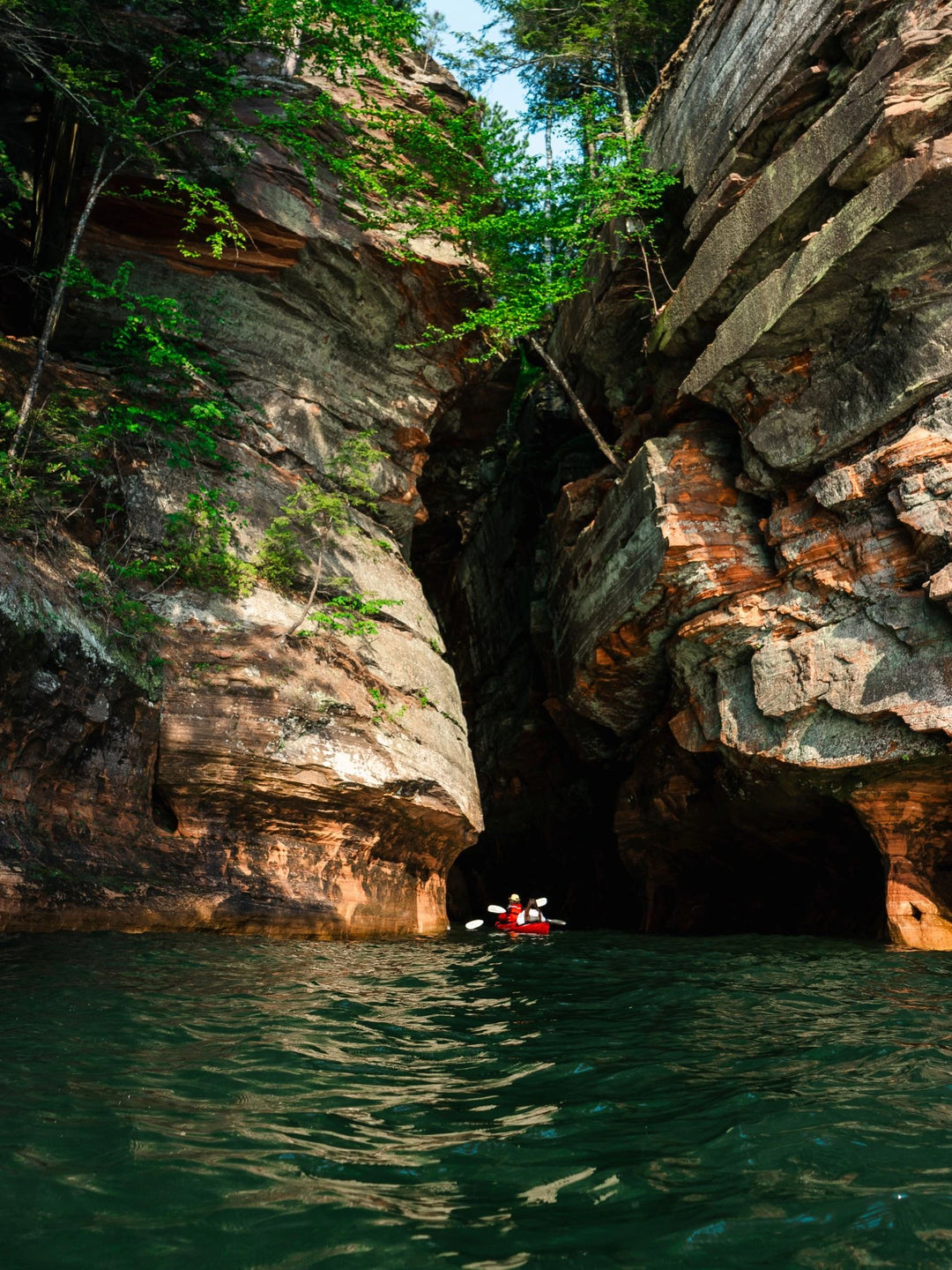 Two people in a sea kayak paddling into a sea cave on blue water. 