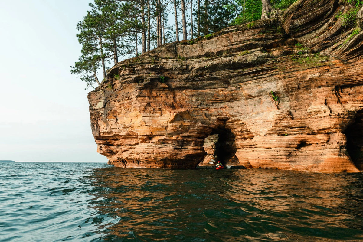 A image of a red rock sea cave with a person paddle boarding under a rock arch