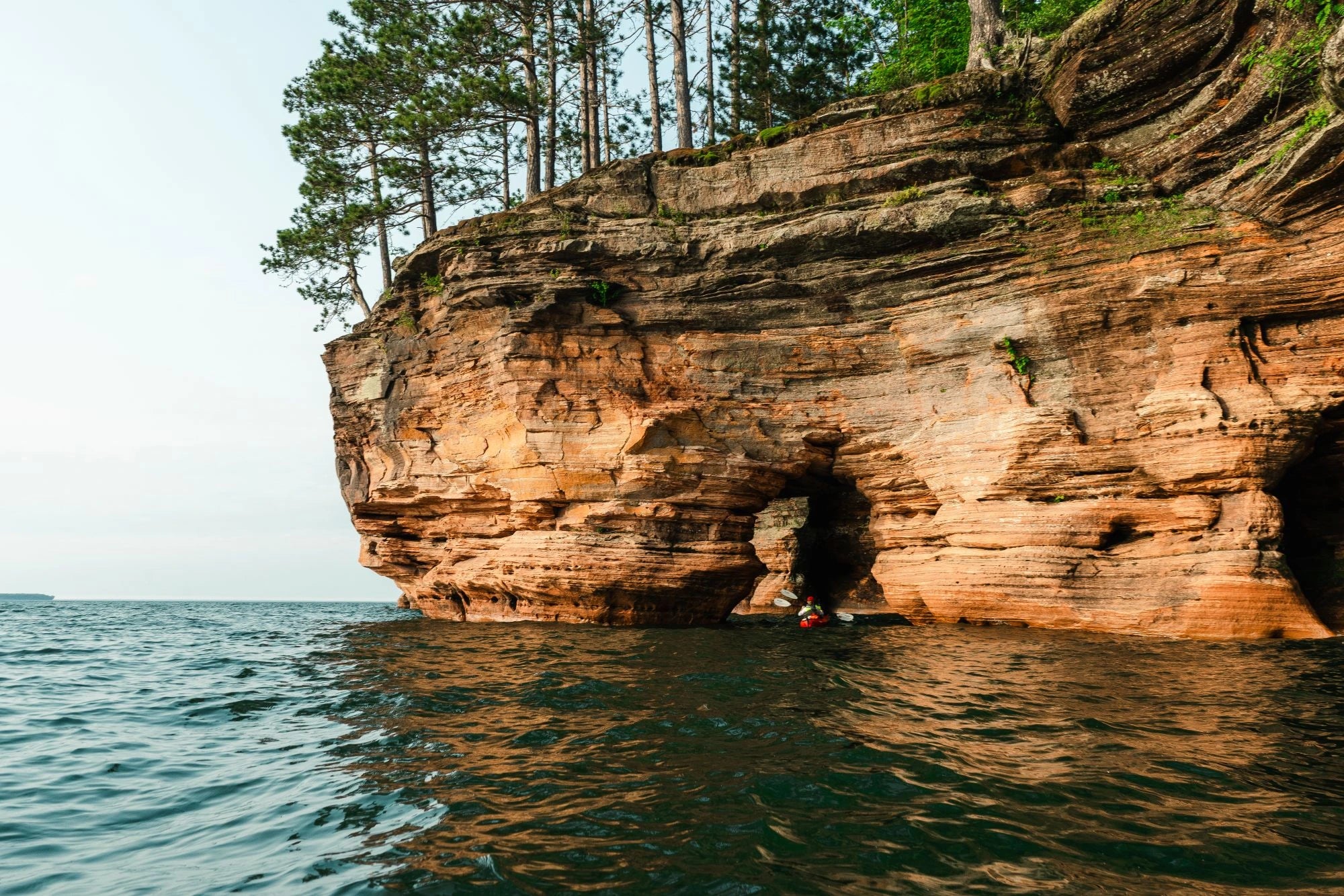 A image of a red rock sea cave with a person paddle boarding under a rock arch