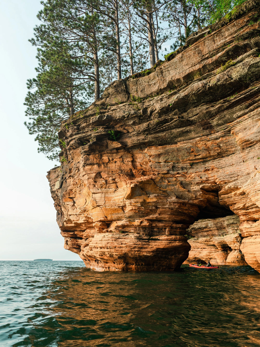 Two people in a kayak paddling under a red rock arch